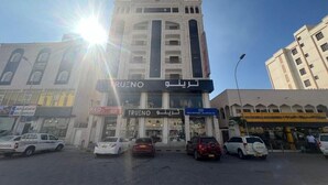 Um edifício de vários andares com um letreiro 'TRUENO' em destaque, rodeado de carros estacionados e outros estabelecimentos comerciais.