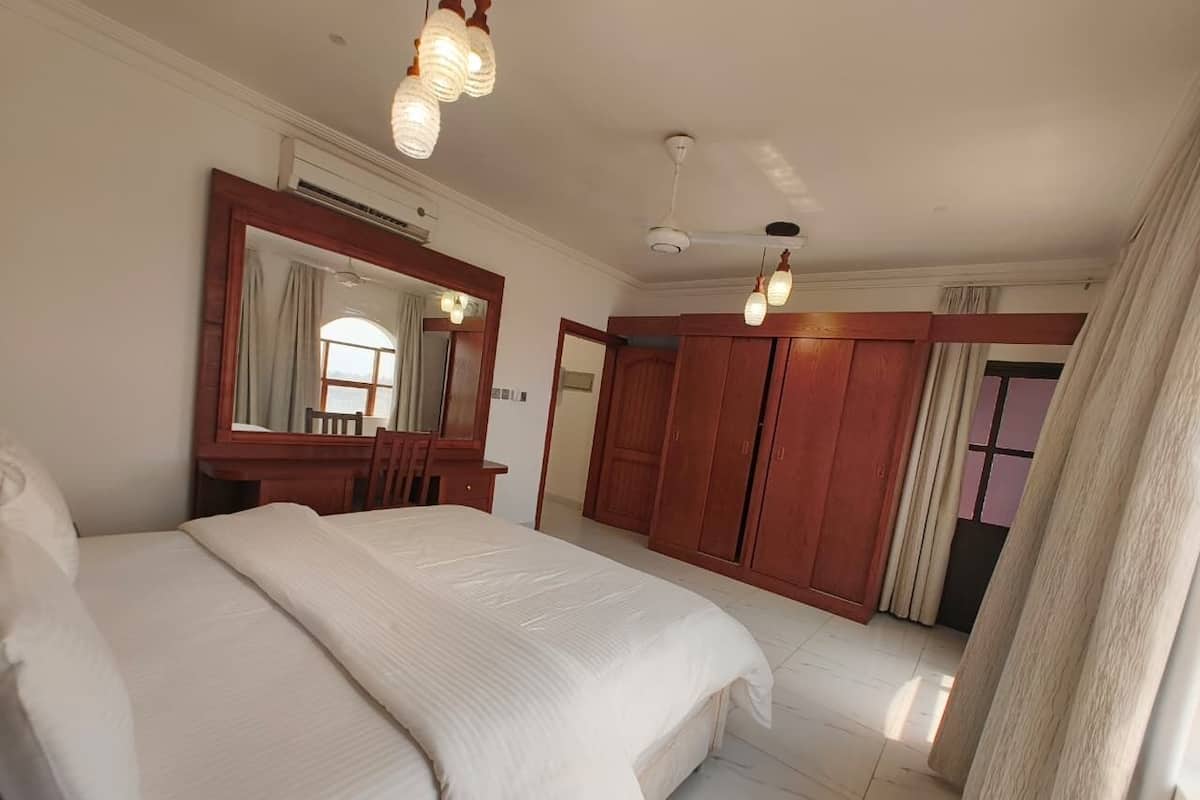 Una habitación de hotel con una cama grande, un armario de madera, un espejo y un ventilador de techo.