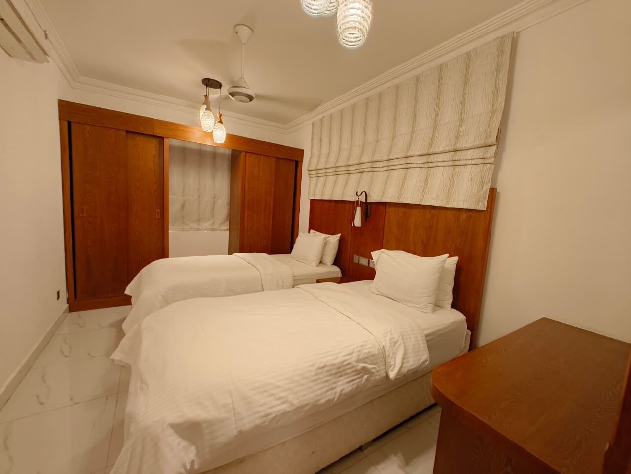 A bedroom with two beds, wooden headboards, a wooden nightstand, and a ceiling fan.