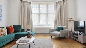 A modern living room with a teal sofa, a grey armchair, a white coffee table, and a flat-screen TV.