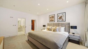 A modern bedroom with a large bed, bedside tables, and framed artwork on the wall.