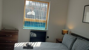 A bedroom with a bed, a dresser, a window with bars, a lamp, and a wall-mounted TV. - Modern 2-bed Apartment -12 Min Walk to Centre (Sheffield)