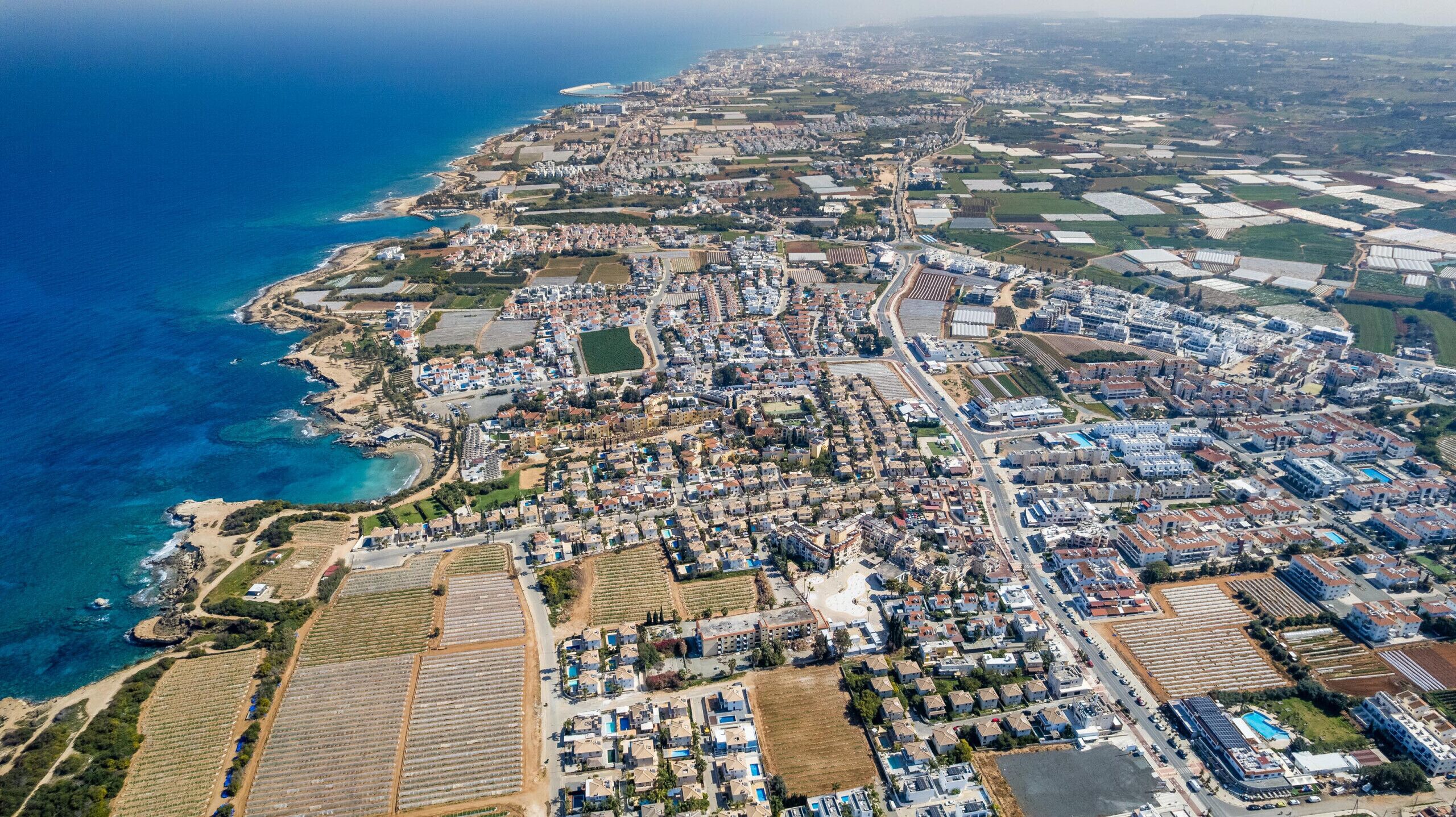 Vista aérea de un pueblo costero con zonas residenciales, campos de cultivo y una playa.