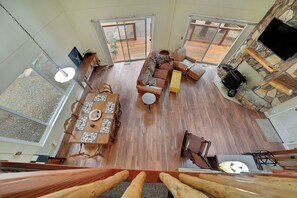 A spacious living area with a wooden floor, a sofa, a coffee table, and a TV mounted on a stone wall. - Cozy 2-bedroom chalet in charming Buckhorn area of Pioneer with WiFi, AC (Pioneer)