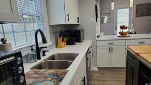 Une cuisine moderne avec des meubles blancs, un évier à deux bacs, un grille-pain et une planche à découper en bois.
