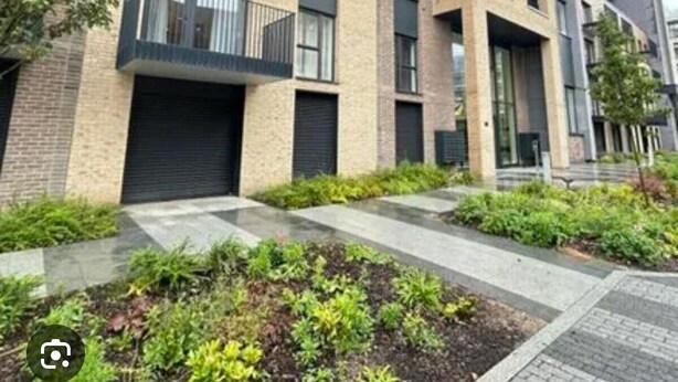 Un moderno edificio residencial de varios pisos con balcones, ventanas amplias y un jardín ajardinado.