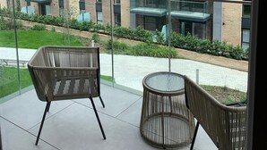 Un moderno edificio de apartamentos con varios balcones, barandilla de vidrio y un patio con mobiliario de mimbre.