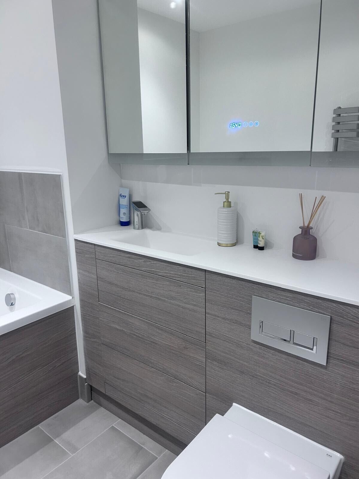 Uma casa de banho moderna com uma pia branca, armários cinzentos e um espelho sobre a bancada.
