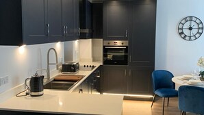 Una cocina moderna con muebles oscuros, una isla central y una zona de comedor con una silla azul.