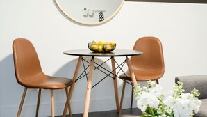 A modern living room with a round mirror, two leather chairs, a small round table with a bowl of fruit, a vase with white flowers, and a wooden side table with a decorative piece. - The Scarlet – Midtown Apt w/ Balcony & Skyline (Atlanta)