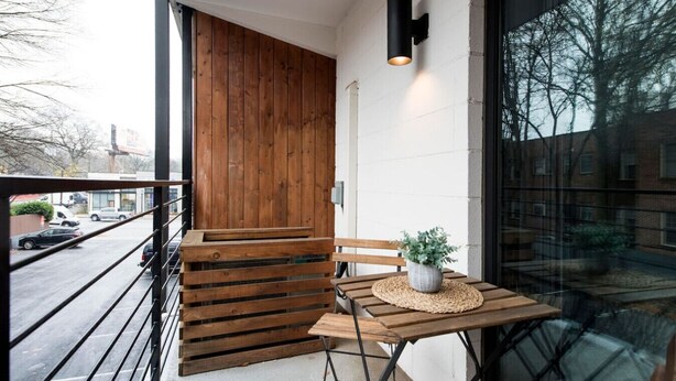 A wooden bench and table on a balcony with a potted plant, overlooking a street. - The Scarlet – Midtown Apt w/ Balcony & Skyline (Atlanta)