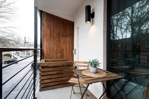 A wooden bench and table on a balcony with a potted plant, overlooking a street. - The Scarlet – Midtown Apt w/ Balcony & Skyline (Atlanta)