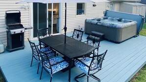 Een terras met een barbecue, een hottub en een tafel met stoelen.