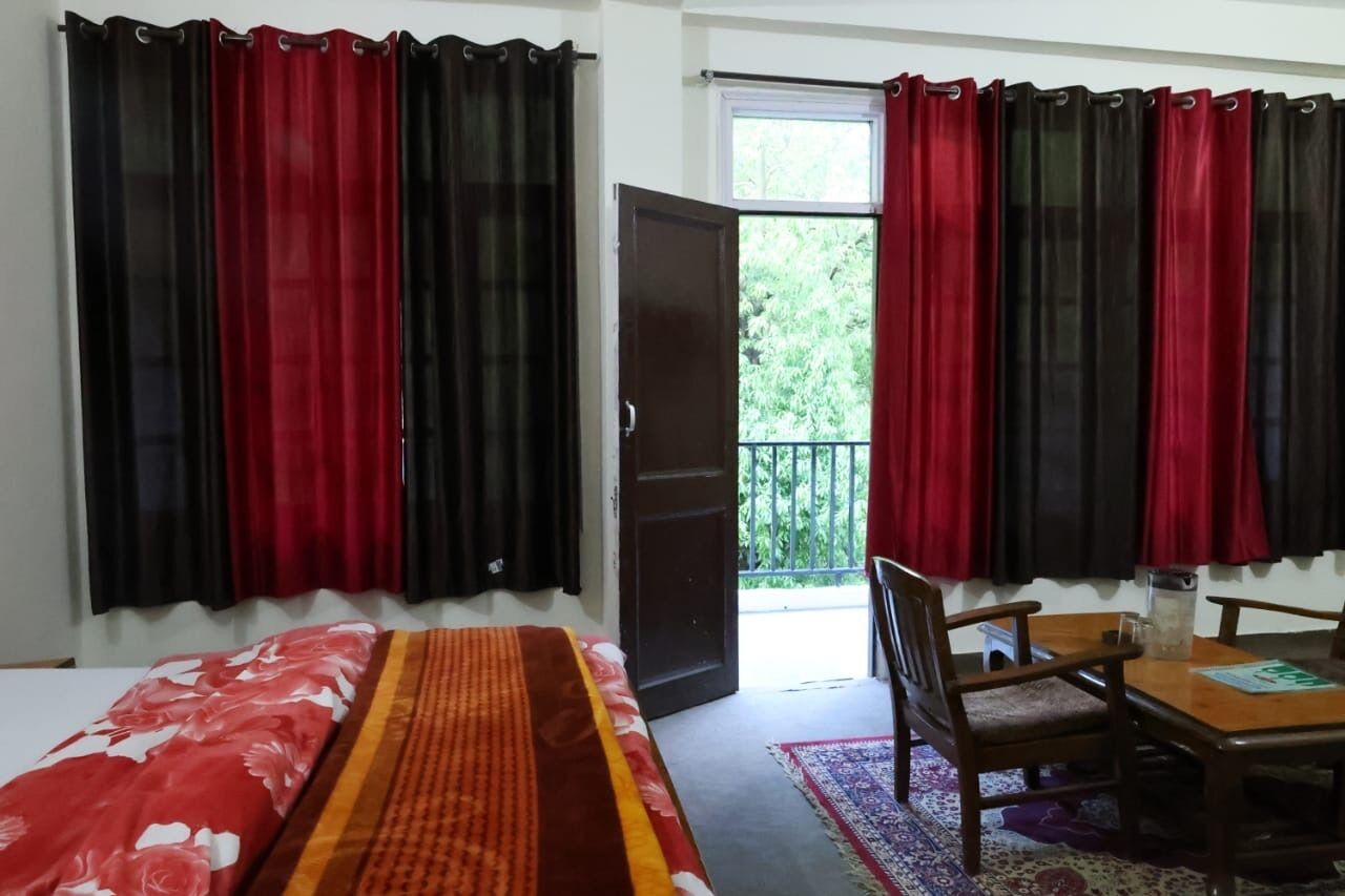 Une pièce comprenant un lit, une table et des chaises, une porte donnant sur un balcon, ainsi que des rideaux rouges et noirs.