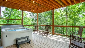 Eine Holzterrasse mit Whirlpool, Holzstühlen und Blick auf einen Wald.