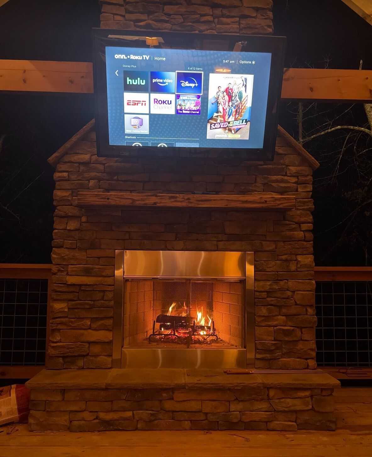 A stone fireplace with a television mounted above it displaying various streaming services.