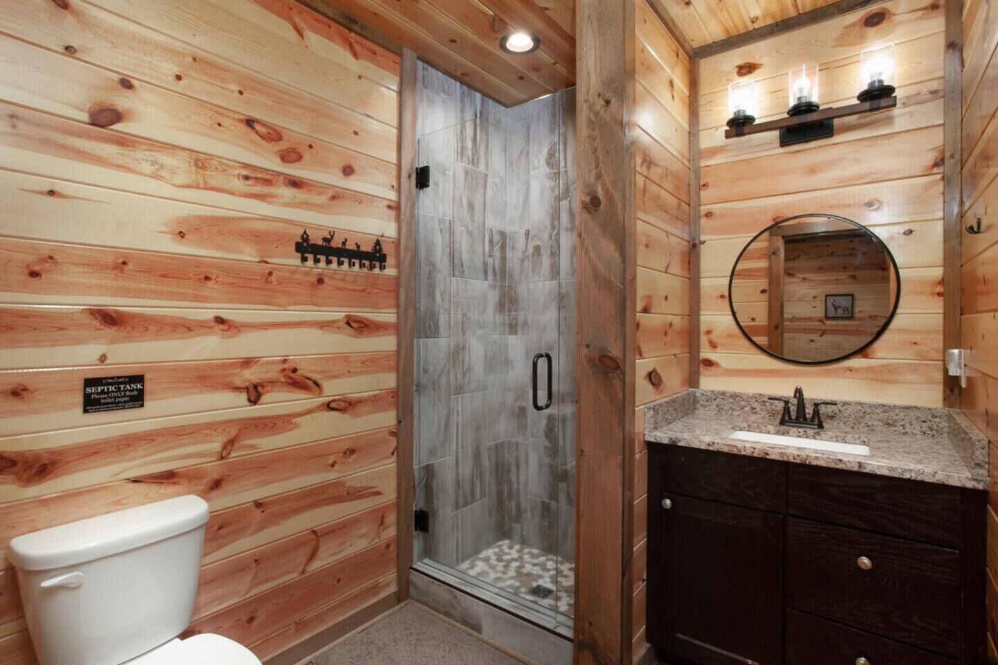 A wooden cabin bathroom with a shower, toilet, vanity, and a sign indicating a septic tank.