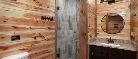 A wooden cabin bathroom with a shower, toilet, vanity, and a sign indicating a septic tank.