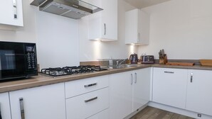 A modern kitchen with white cabinets, a gas stove, a microwave, and a toaster. - 37 Devana Gardens (Chester)