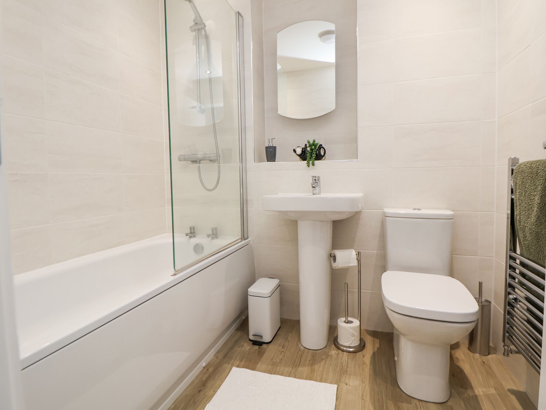 Un baño moderno con ducha de vidrio, lavamanos pedestal y retrete.