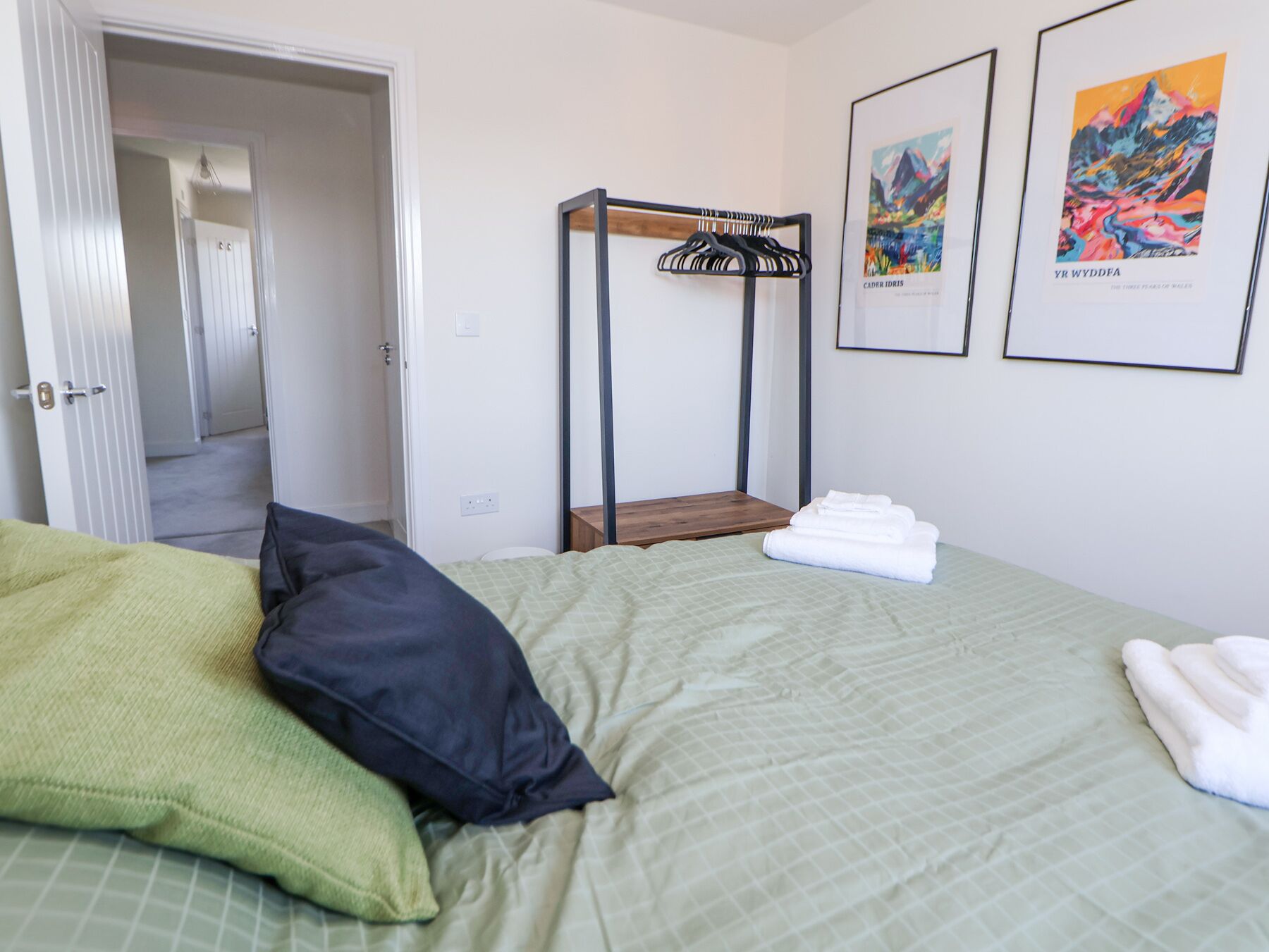 Ein Schlafzimmer mit einem Bett, Kissen, einem Holzregal und zwei gerahmten Bildern an der Wand.