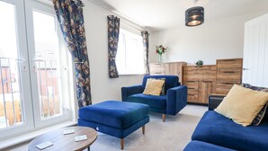 A modern living room with a blue sofa set, a wooden cabinet, and a round coffee table. - 37 Devana Gardens (Chester)