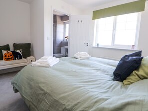 Un dormitorio con cama, un banco con almohadas, un inodoro y una ventana.