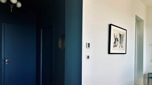 A hallway with a dark blue door, a white wall with a framed artwork, and a light switch. - JADE (double room with sitting area) (CARCASSONNE)