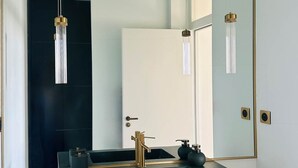 A modern bathroom with a large mirror, a black countertop, a gold faucet, and a hanging light fixture. - JADE (double room with sitting area) (CARCASSONNE)