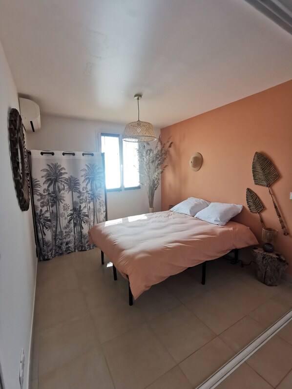 Un dormitorio con cama, ventana, lámpara colgante y aire acondicionado instalado en la pared.