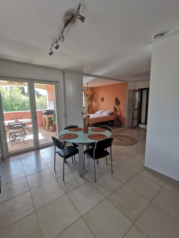 Un comedor con una mesa y sillas, una lámpara en el techo y vistas a un dormitorio con cama y ventana.