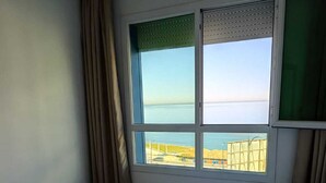 Ein Hotelzimmer mit zwei Betten, einem großen Fenster mit Meerblick und einem grünen Vorhang.