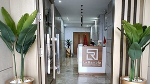 Ein Hotel-Rezeptionsbereich mit modernem Design, inklusive einer Rezeption mit der Aufschrift 'La Rambla Residence Touristique'. An beiden Seiten des Eingangs befinden sich Blumentöpfe, und der Boden ist mit Marmor ausgelegt.