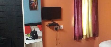 Quarto de hotel com cama, escrivaninha com computador, ar-condicionado e televisão.