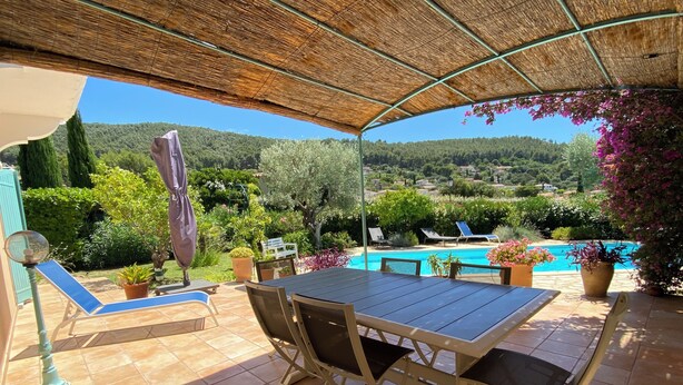 An outdoor patio with a table and chairs, a pool, and surrounding greenery.
