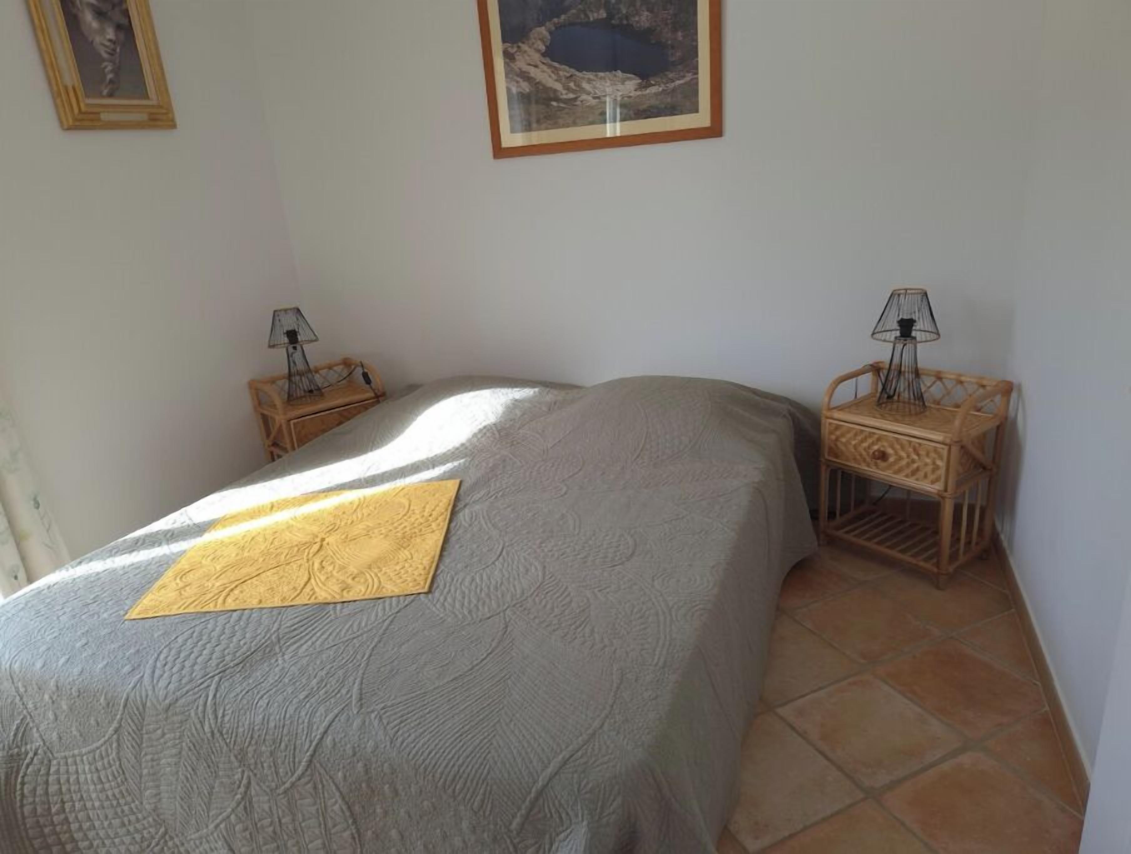 Quarto com uma cama, duas mesas de cabeceira, uma lâmpada em cada e um quadro na parede.