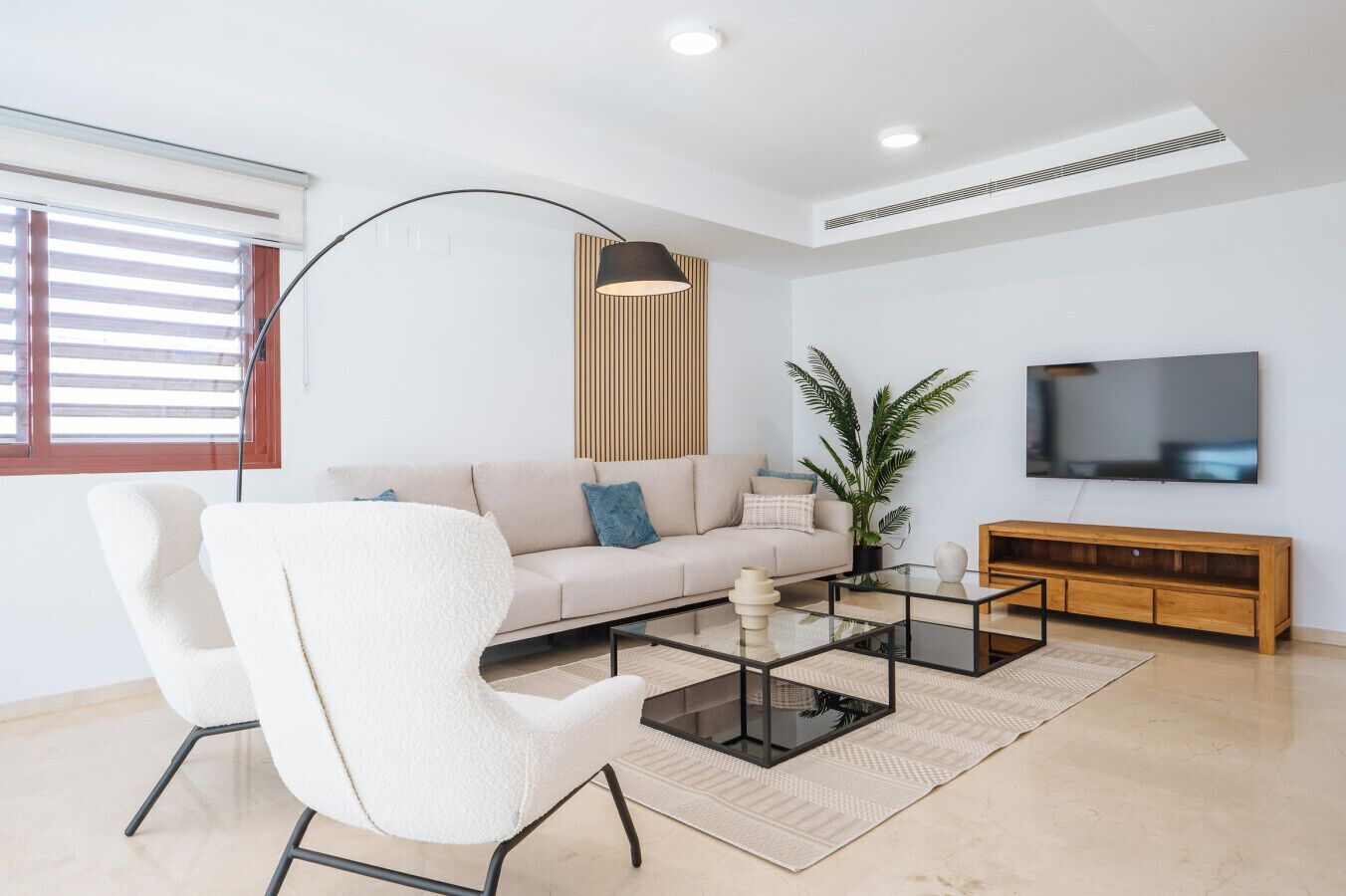 A modern living room with a sofa, a white armchair, a coffee table, a TV, and a wooden cabinet.