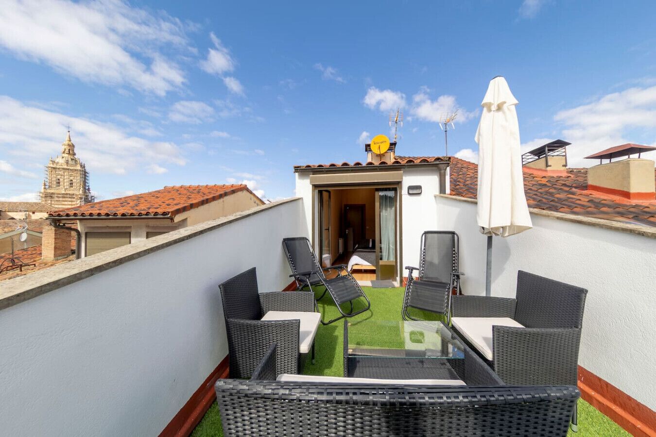 A rooftop terrace with outdoor furniture, a small table, and a view of a historic building in the background.