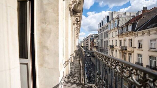A balcony with ornate metal railings overlooking a street with historic buildings.