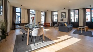 A spacious living room with a dining area, large windows, and modern furniture.