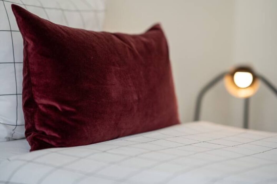 A bed with a white mattress and a dark red pillow.