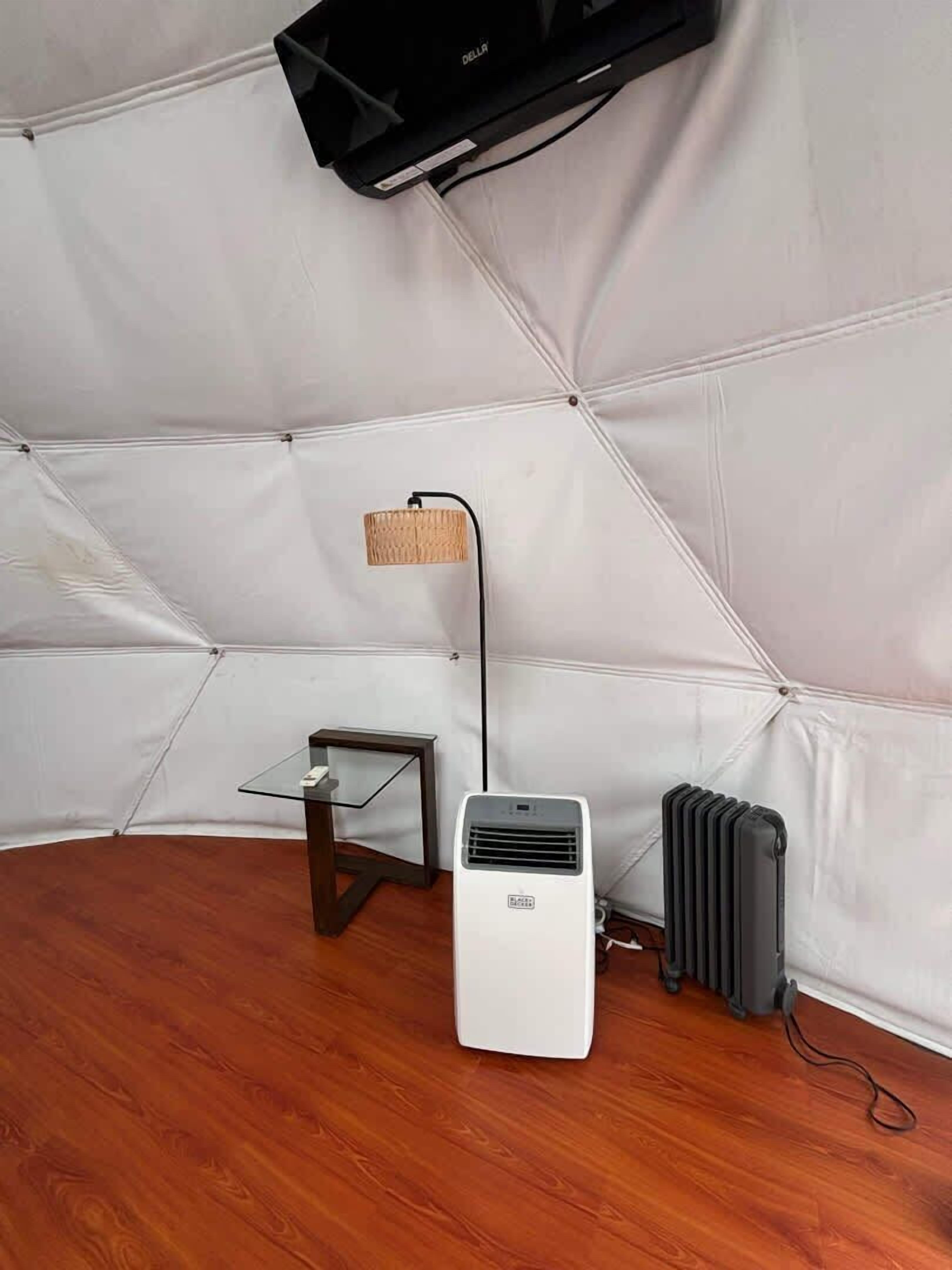 A room with a white air conditioner, a small table with a glass top, a wicker lamp, and a radiator.