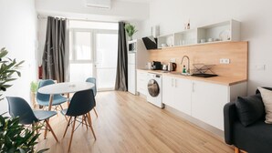 A modern kitchen with a washing machine, a dining area with a round table and chairs, and a sofa. - Stylish Studio with Easy Access to Valencia's Best (València)