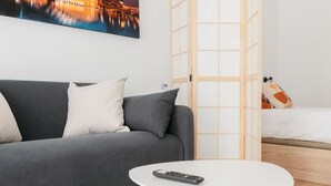 A modern hotel room with a grey sofa, a white table, and a bed with colorful pillows. - Stylish Studio with Easy Access to Valencia's Best (València)
