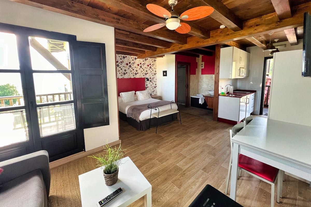 Una habitación pequeña con cama, kitchenette, comedor y balcón.