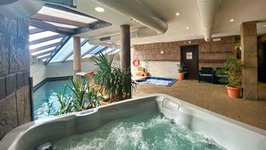 An indoor swimming pool with a hot tub, surrounded by stone walls and potted plants. - Apartamentos Spa Casco Histórico de Isla (Isla)