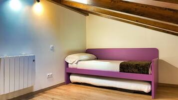 A small, single-bed room with a purple headboard, a white mattress, and a brown blanket. There is a white radiator on the left and a wooden ceiling with exposed beams.