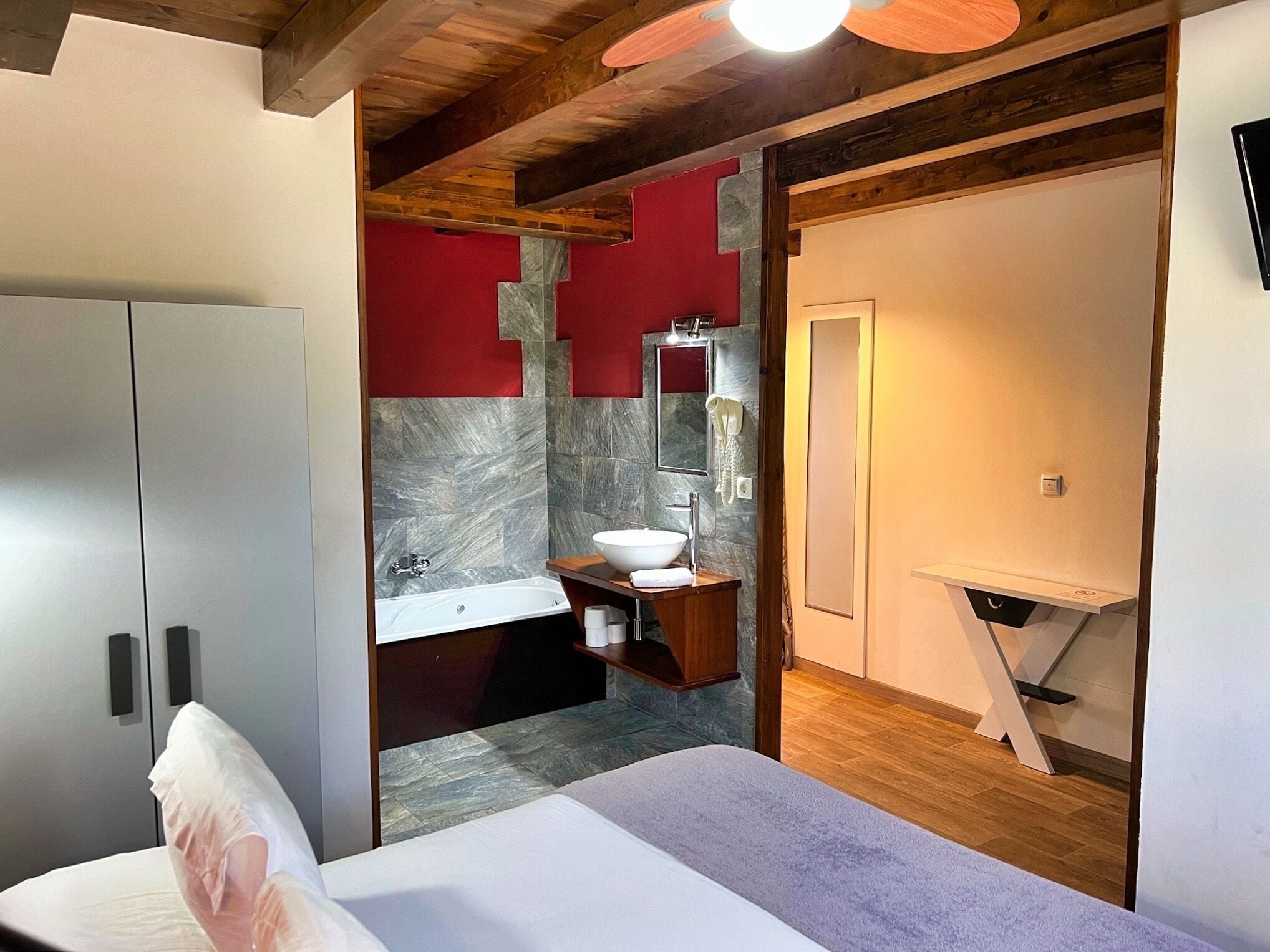 A modern bathroom with a marble wall, a wooden vanity, a white sink, and a large mirror.