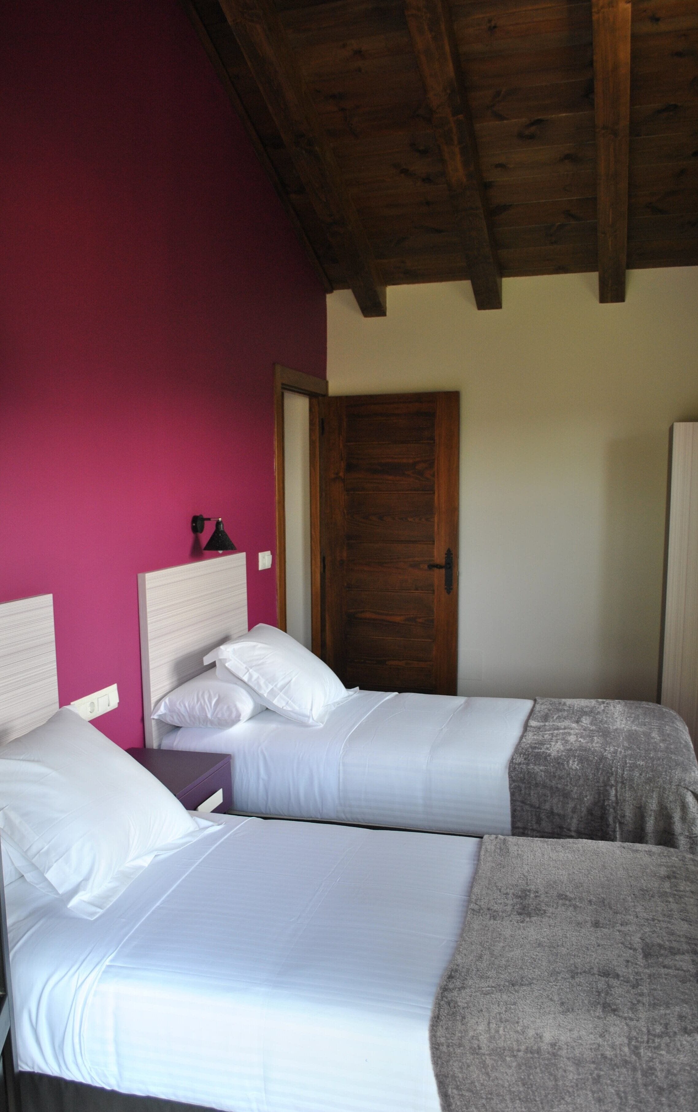 Una habitación con dos camas, techo de madera y una puerta.