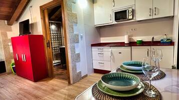 A kitchen with white cabinets, a red refrigerator, a microwave, and a dining table set with plates and glasses.